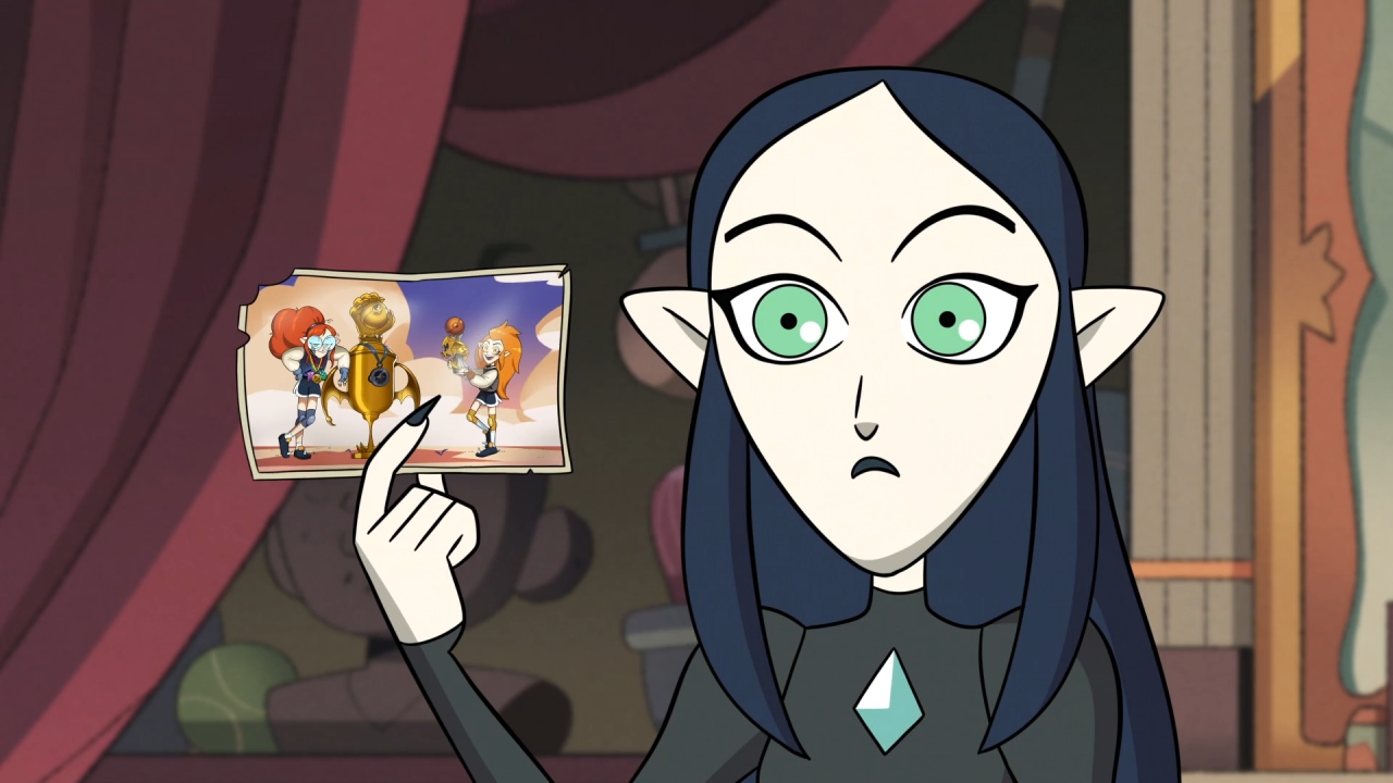 A screenshot from Wing It Like Witches, with Lilith holding up a photo of her and Eda from their grudgby days.